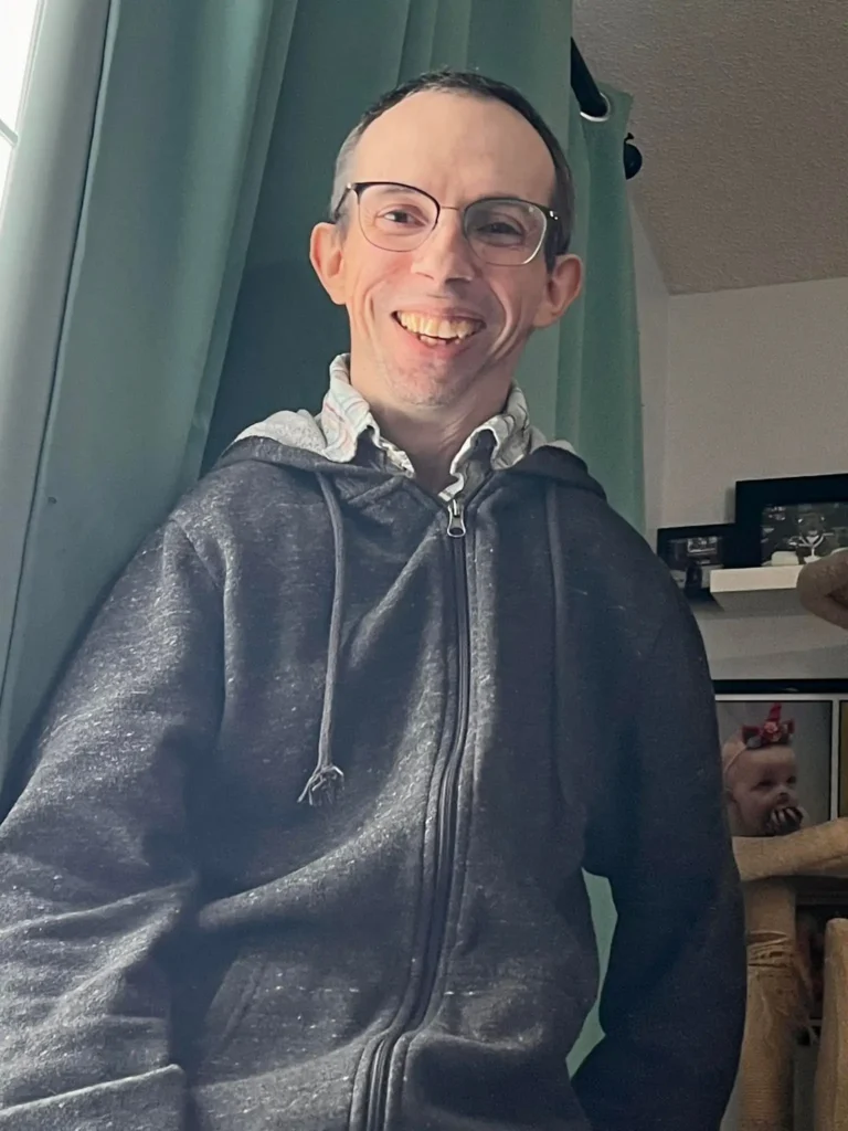 a 45 yo male in a gray hooded sweatshirt sitting in front of teal curtain